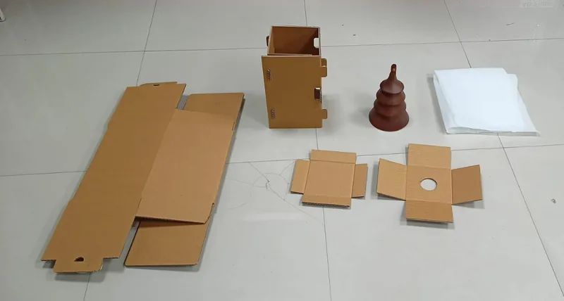 Flat corrugated blanks, a folded box, inserts and a wooden ornament laid out on a floor