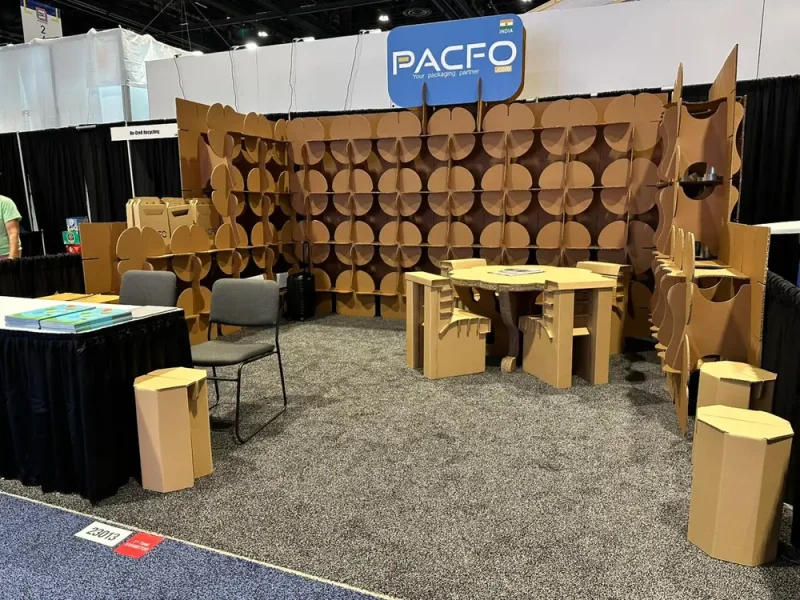 Trade show booth built from cardboard, with modular display walls, a table, chairs and stools