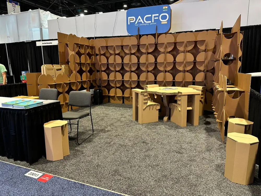 Trade show booth built from cardboard, with modular display walls, a table, chairs and stools